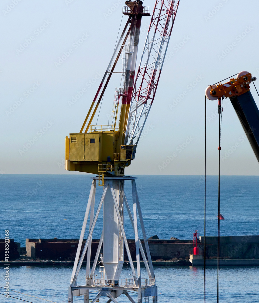 Fototapeta premium Yellow port crane on the quay with breakwater in the background
