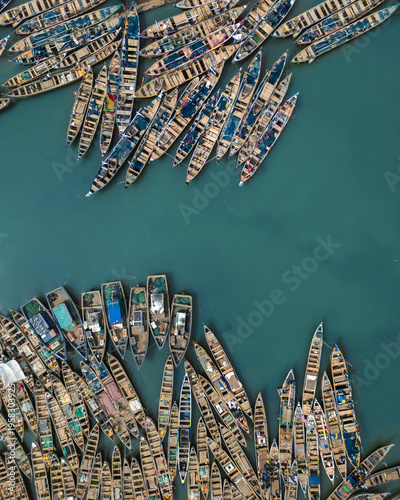 Aerial view of numerous boats clustered tightly on the water, a vibrant tapestry of wood against the turquoise sea, Sekondi Takoradi, Ghana.