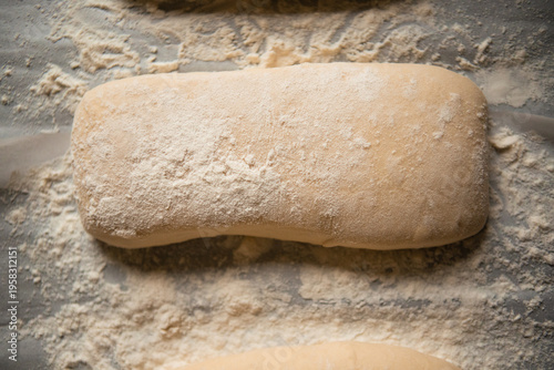 Close-up of raw ciabatta dough generously dusted with flour on a baking surface before going into the oven. Artisan bread preparation process, rustic style, soft natural lighting.