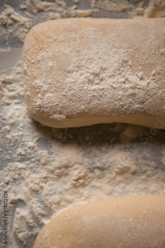 Close-up of raw ciabatta dough generously dusted with flour on a baking surface before going into the oven. Artisan bread preparation process, rustic style, soft natural lighting.
