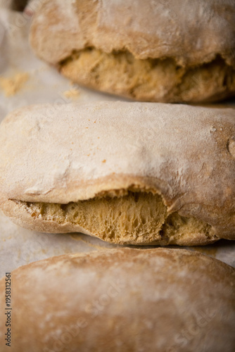 Golden brown ciabatta bread loaves fresh from the oven, dusted with flour and placed on parchment paper. Rustic homemade bakery scene with warm tones and soft textures.