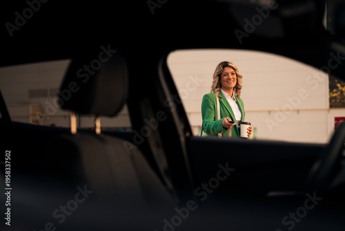 Smiling woman unlocking car while holding coffee cup