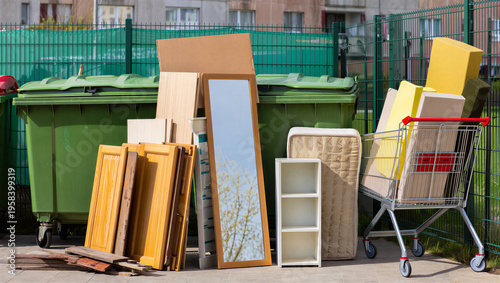 Old furniture and bulky household items stacked near outdoor trash bins for waste collection.
