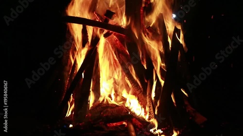 A close-up shot of a burning campfire at night with warm, golden flames and a dark background