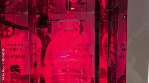 A close-up of a transparent bottle illuminated by red light. The background features abstract shapes and text, creating a modern and artistic atmosphere.