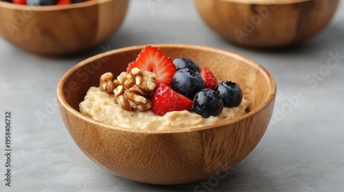 Wooden bowls of oatmeal topped with fresh berries and walnuts