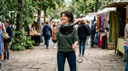 Woman chef juggling kitchen utensils outdoor. Professional cook performing show with pan, knife and ladle in street market. Creative culinary performance and multitasking concept.