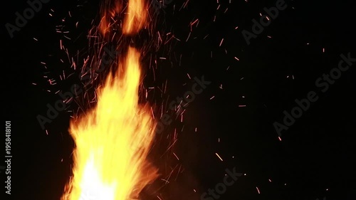 A close-up shot of a vibrant campfire flame against a dark background with sparks flying