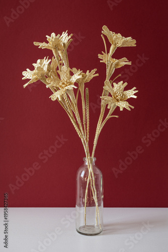 A glass vase with a bouquet of flowers made from straw on the red background. Straw weaving