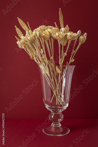 A glass vase with a bouquet of flowers made from straw on the red background. Straw weaving