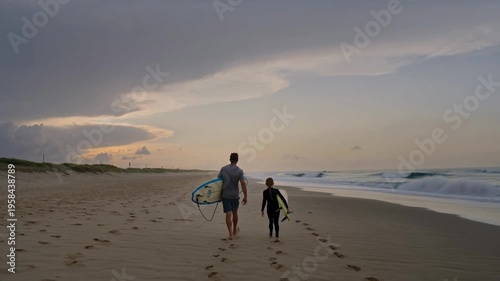 Parent and child walking along sandy beach carrying surfboard, leaving footprints at sunset, expressing bonding and coastal adventure.