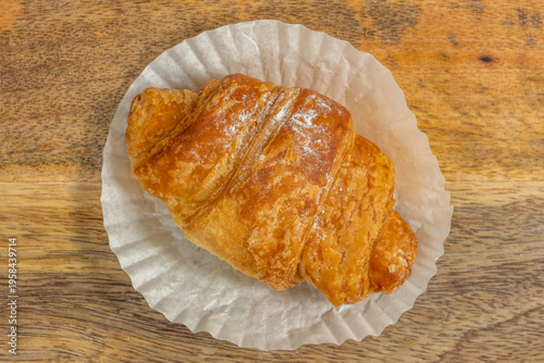 Sweet croissant on paper and wood background.