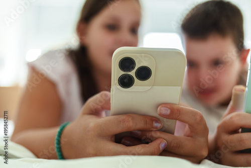 Boy and girl using smart phones in their room. Two kids learn use devices together lying on bed.