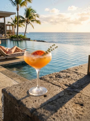 A refreshing cocktail sits on a stone ledge by a pool. In the background, a person relaxes on a lounge chair under palm trees. The scene captures a tropical vacation vibe.