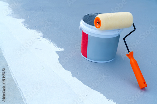 Foto Orange paint roller resting on a bucket of grey liquid coating on a rooftop or floor