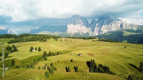 Alpine meadow with farmhouses and mountain range under clouds. Seiser Alm Italian Dolomites
