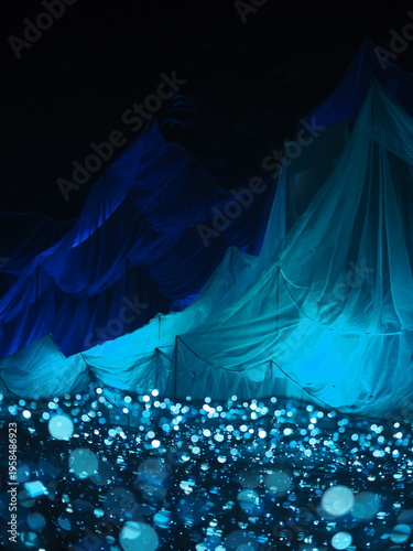 A bride in a flowing blue dress creates a smooth motion pattern as soft smoke and light curve into a fractal wave against a dark backdrop