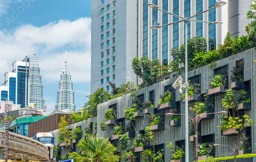 Monorail train passing through central Kuala Lumpur along modern buildings with vertical gardens and green facades. Urban transport infrastructure, sustainable design and city development, Malaysia