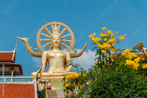 Golden Big Buddha statue at Wat Phra Yai temple framed by yellow flowers on Koh Samui island Thailand
