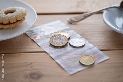 British pound sterling banknotes and coins on table with cookie and coffee cup nearby casual dining setting in cafe, UK pound currency beside snack, hospitality tipping, daily life, financial services