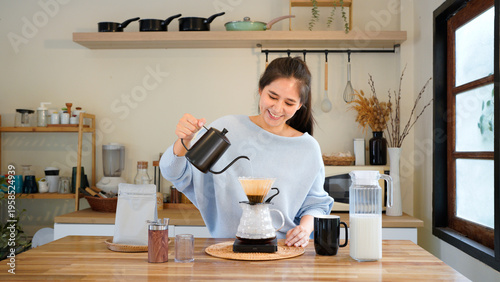 Young asian woman pouring hot water from black kettle into coffee dripper, Female brewing drip coffee in modern kitchen, Morning lifestyle, slow bar cafe and home brewing concept