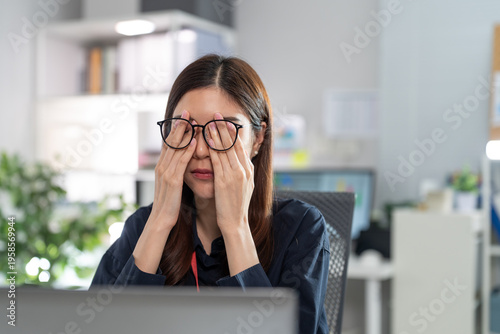 Foto Tired Asian businesswoman rubbing eyes suffering from eye strain after long hours working with laptop computer in office