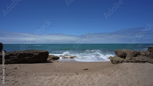 Small Secluded Rocky Beach in Chiclana de la Frontera Spain; Scenic Atlantic Ocean Waves Crashing on Sand at La Barrosa Coast in Andalusia with Blue Sky and Turquoise Water Establishing Shot