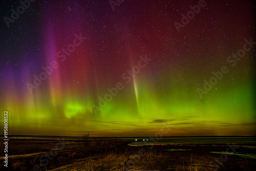Vivid northern lights dancing over a calm shoreline beneath a star-filled night sky with colorful aurora glow.