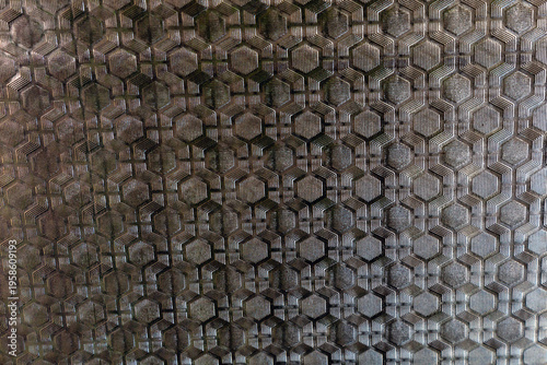 Textured patterned window glass with geometric hexagonal design, abstract background with metallic look, modern architectural surface with copy space.