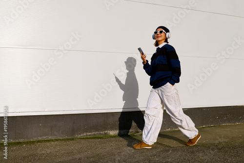 Obraz na plátne Woman walking listening to music using smartphone and headphones