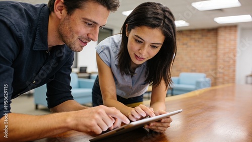Diverse Young Professionals Collaborating in Modern Office: Focused Man and Woman Using Tablet for Creative Project in Bright Industrial Shared Workspace