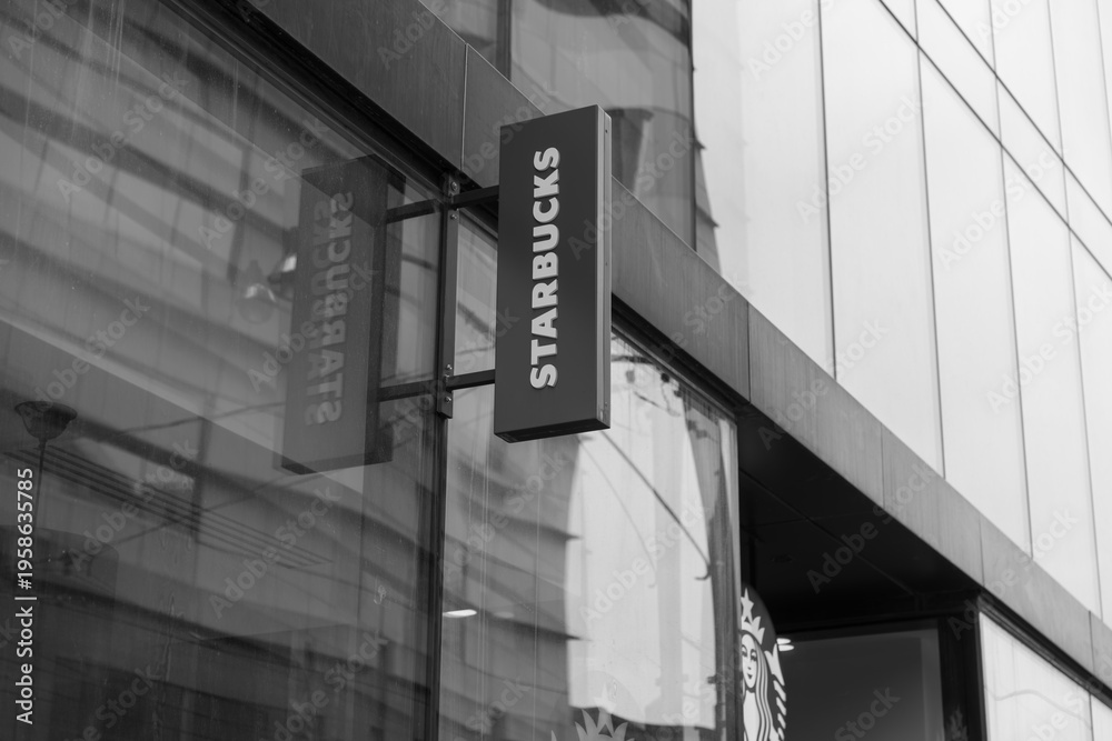 Fototapeta premium black and white view of building exterior and projecting sign of Starbucks Coffee Company, a coffee shop chain, located here at 221 Queen St W, Smart House Condo, Toronto