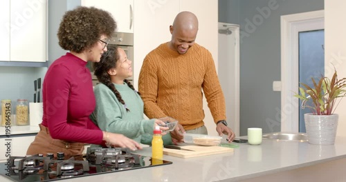 After father finishes slicing sandwich, diverse family packing daughter's lunch at kitchen island