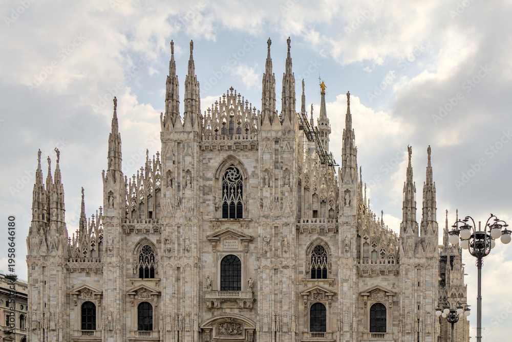 custom made wallpaper toronto digitalThe Duomo di Milano with its white marble Gothic façade, dense with statues, pointed arches, and tall spires. Shot from the square below, cathedral rises dramatically beneath soft, clouded sky.