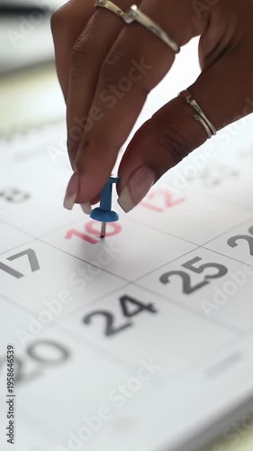 Close-up flat lay video of diverse hands marking dates on a white desk calendar with red & blue pushpins against blurred office. Strategic planning and goal achievement