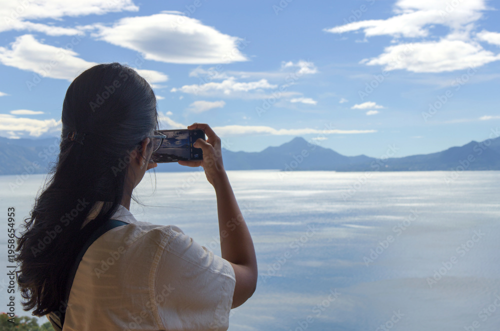 custom made wallpaper toronto digitalWoman taking a photo of volcanos and mountains at lake atitlan from a restaurant patio. travel, exploration, and nature appreciation