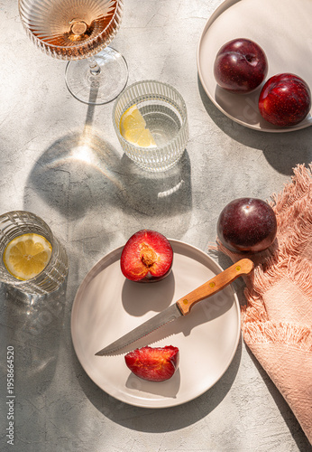 Summer table set with fruit. Two plates of plums, water with lemon, wine.  Sunny day. Top view.