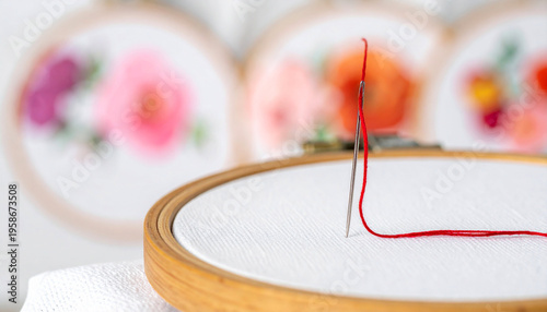 Close up of silver needle pulling bright crimson thread through white fabric in embroidery