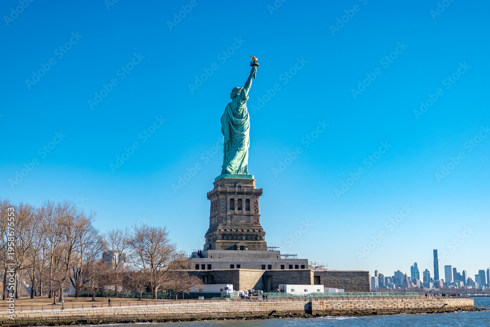 Fototapeta premium Rear view of the Statue of Liberty standing on Liberty Island under a clear blue sky in New York Harbor, USA. Iconic national landmark, travel destination and freedom concept.