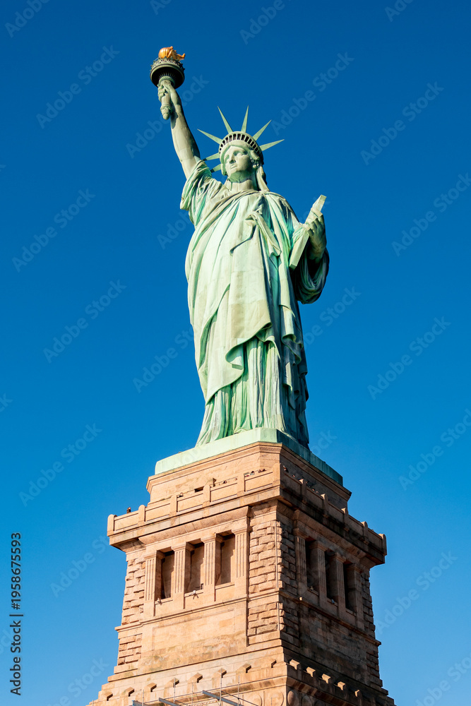 Fototapeta premium Low-angle full view of the Statue of Liberty standing on its pedestal under a clear blue sky on Liberty Island in New York Harbor, USA. 
