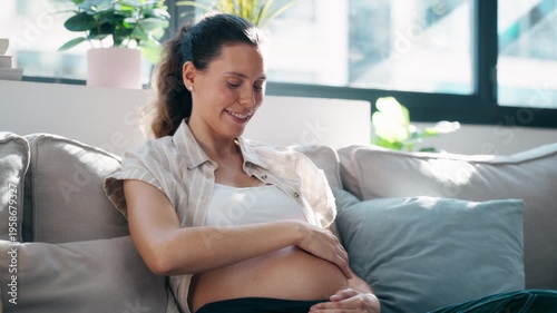 Video of pregnant woman touching her belly to feel the baby's movements while sitting on the couch at home