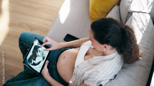 Video of pregnant woman looking at a baby ultrasound sitting on the couch at home