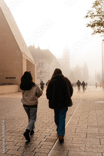 Two people walking along a misty Liechtenstein European city street in soft morning light. Calm urban atmosphere with historic architecture creates a peaceful lifestyle and travel concept.
