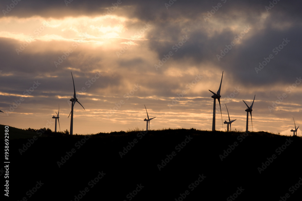 Fototapeta premium Wind turbines silhouetted against a dramatic sunset sky