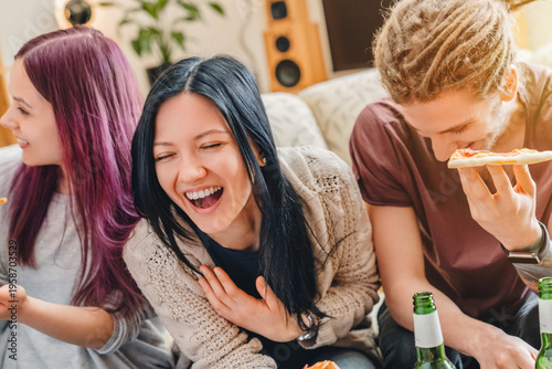 Canvas Print Happy young friends eating pizza and drinking beer on sofa at home, enjoying wee