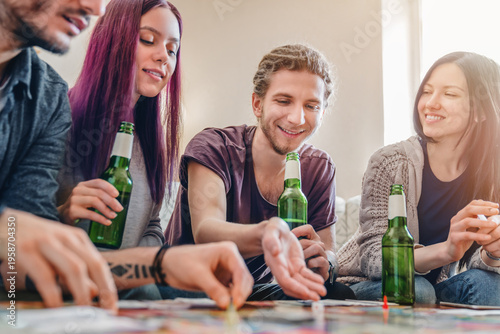 Canvas Print Group of young people playing a board game at home, drinking beer, sitting on co