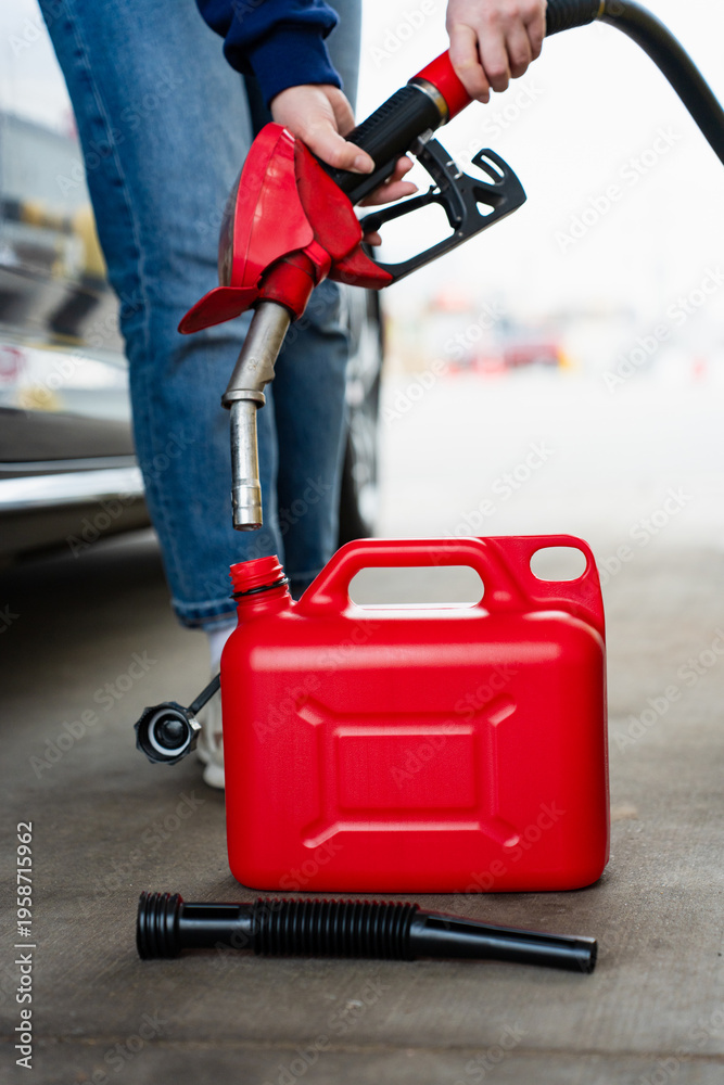 Fototapeta premium Gasoline flowing from fuel pump nozzle into red plastic canister.