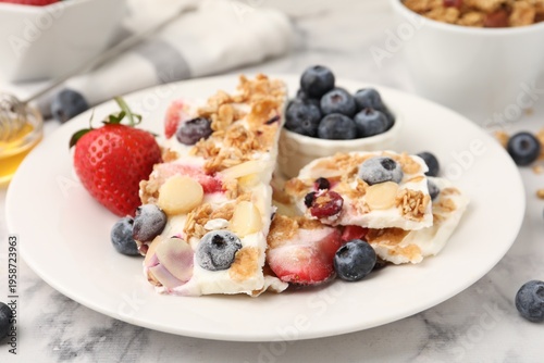Foto Pieces of tasty yogurt bark with berries, almond flakes and granola on white mar