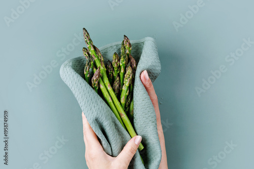 Woman holding fresh asparagus in hands wrapped with kitchen towel on soft green background