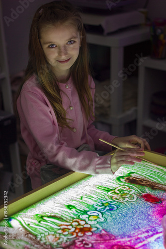 Beautiful little girl draws with sand on a light square, art therapy, sand animation, creative leisure for children, selective focus